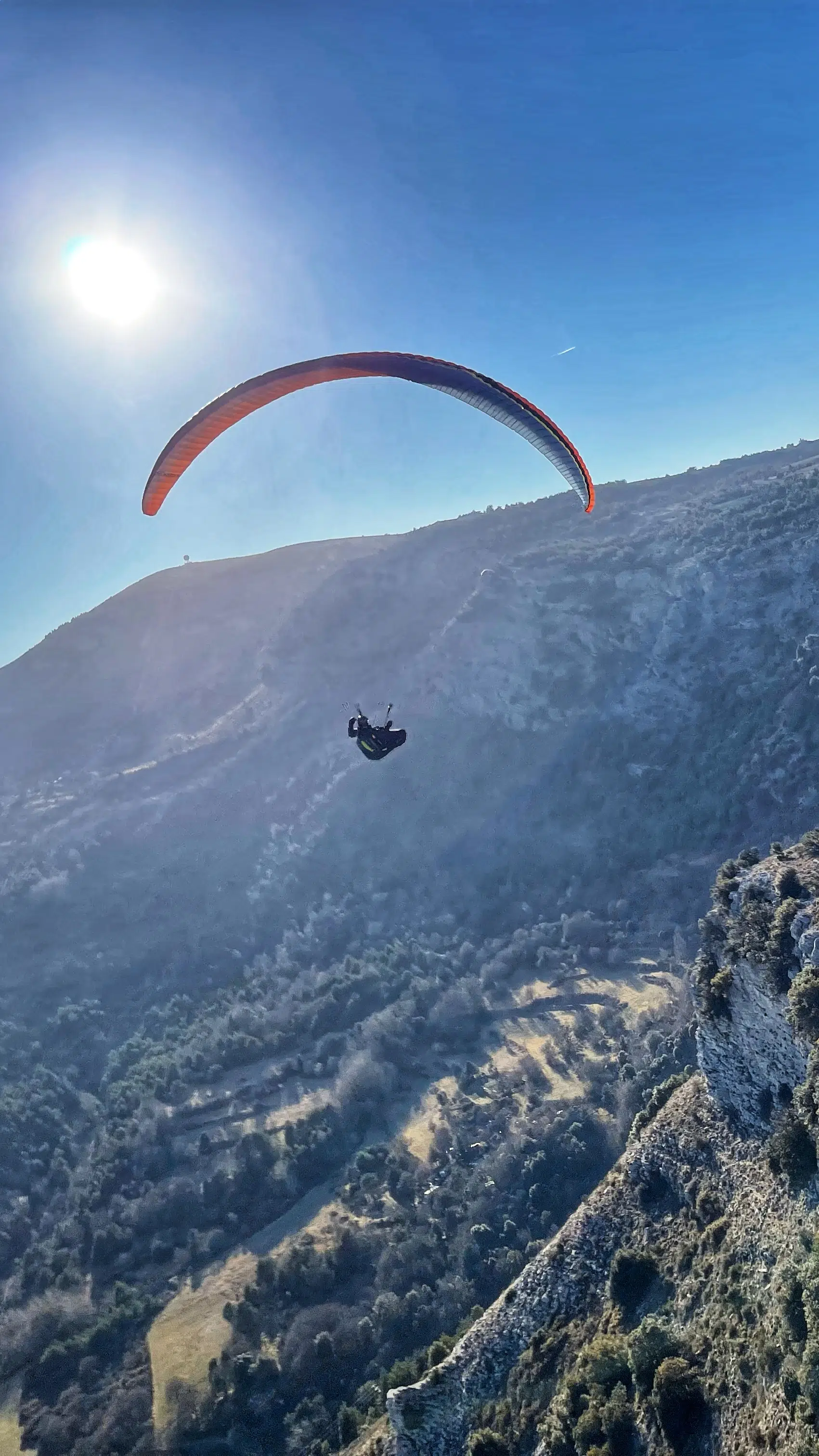 Parapentist flying solo working the air above a sunny landscape of the Southern Alps