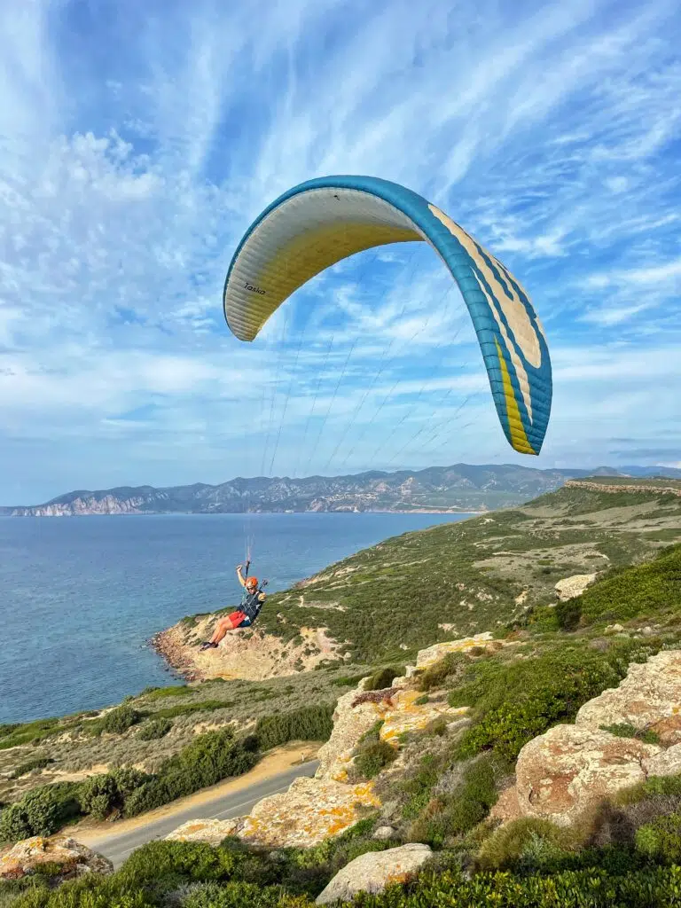 Pilot installed in their paragliding harness in flight above the coast, legs extended