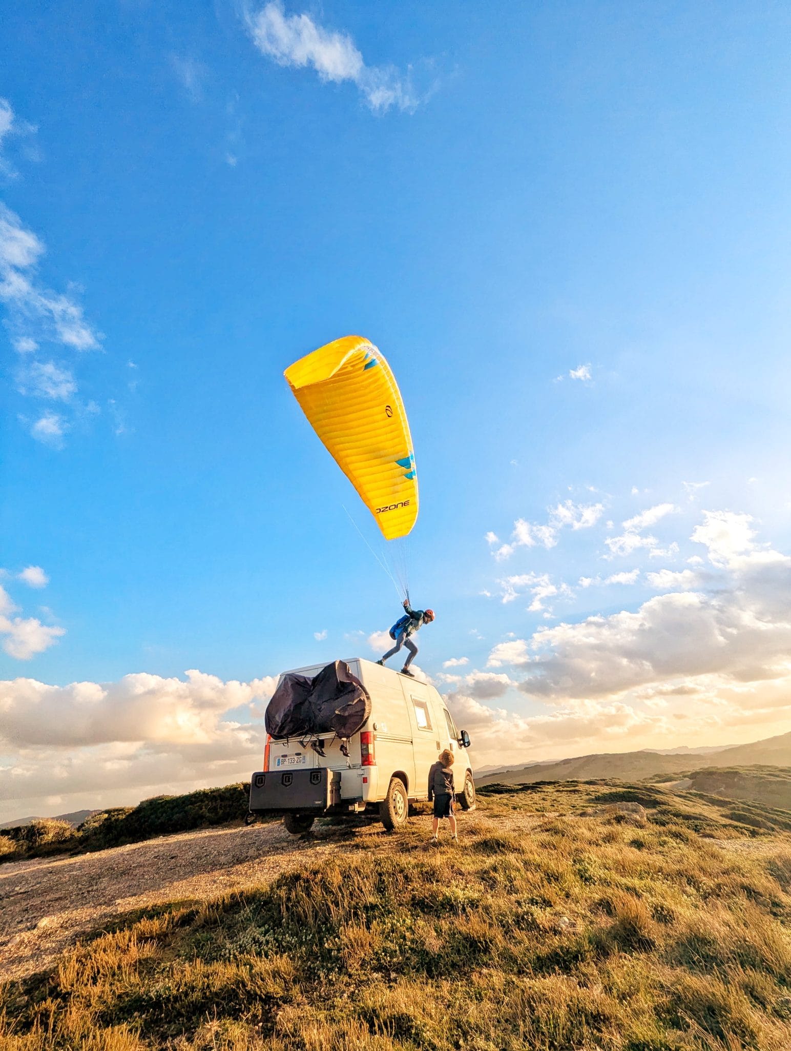 Pilote suspendu dans sa sellette de parapente au décollage, lumière dorée de fin de journée